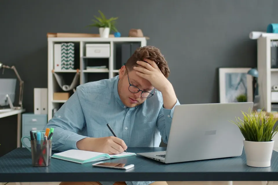 Dirigeant à son bureau, la tête dans la main, devant son ordinateur et ses notes